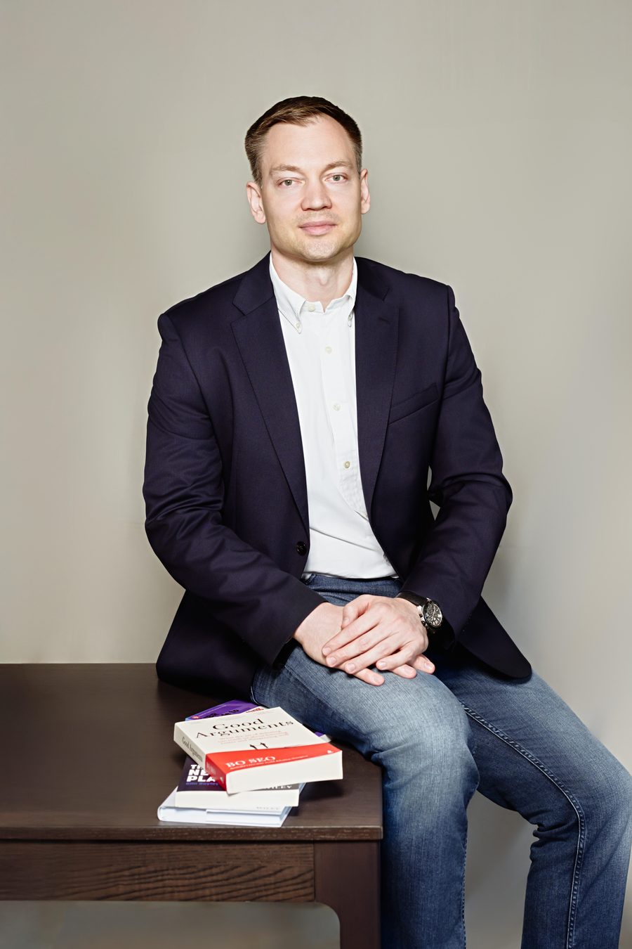 Alex Mironov, in a navy blazer, seated at a desk with books